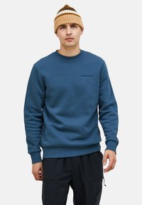 Felpa di cotone blu con collo rotondo e polsini a costine. Presenta un piccolo logo ricamato sul petto ed è abbinata a un berretto a maglia a righe.