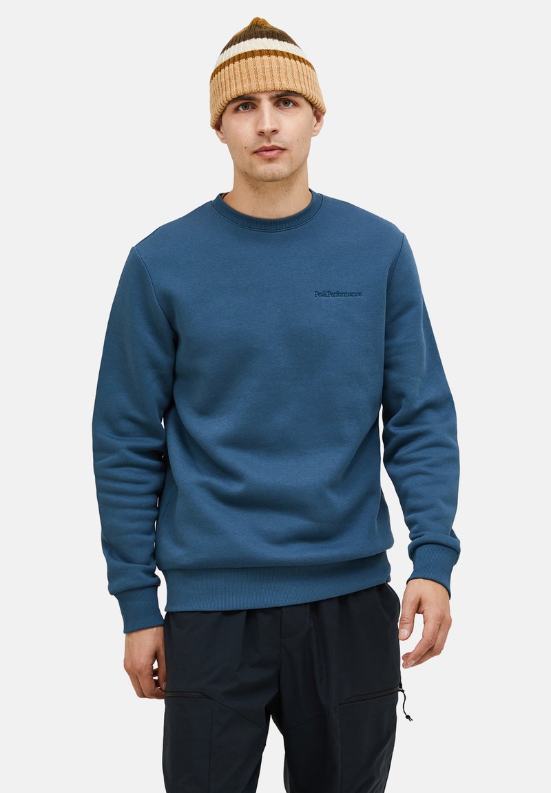 Felpa di cotone blu con collo rotondo e polsini a costine. Presenta un piccolo logo ricamato sul petto ed è abbinata a un berretto a maglia a righe.