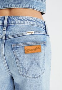 Gaiši mazgātas džinsa bikses ir aprīkotas ar ādas birku uz aizmugurējā kabatas ar "Wrangler" zīmolu, veidotas ar kontrastējošu šuvju un klasisku griezumu.