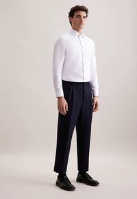 Wit shirt met lange mouwen, een puntige kraag en knopen aan de voorkant, gecombineerd met marineblauwe op maat gemaakte broek en zwarte leren schoenen, model staand.