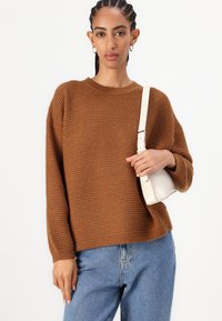 Brown ribbed knit sweater with a relaxed fit. Paired with high-waisted light blue jeans and a small cream handbag.