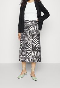 Gonna midi a stampa zebra bianco e nero realizzato in tessuto leggero, abbinato a un top bianco aderente e scarpe ballerine verde menta con lacci alla caviglia.