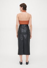 Bruine haltertop en zwarte leren midi-rok met split aan de achterkant, met twee achterzakken en een getailleerd ontwerp. Zwarte gespen schoenen.