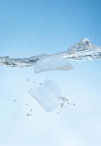 To transparente, hvide geléagtige former flyder i klart vand, med bobler og en glat tekstur, mod en lyseblå baggrund.