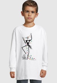 T-shirt bianco a maniche lunghe con un'illustrazione nera di una figura decorata con luci di Natale colorate. Sotto c'è la scritta "The Nightmare Before Christmas".