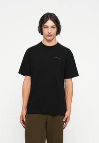 Svart bomull t-skjorte med korte ermer, rund hals, og en liten hvit trykt logo på brystet. Glatt tekstur, avslappet passform.