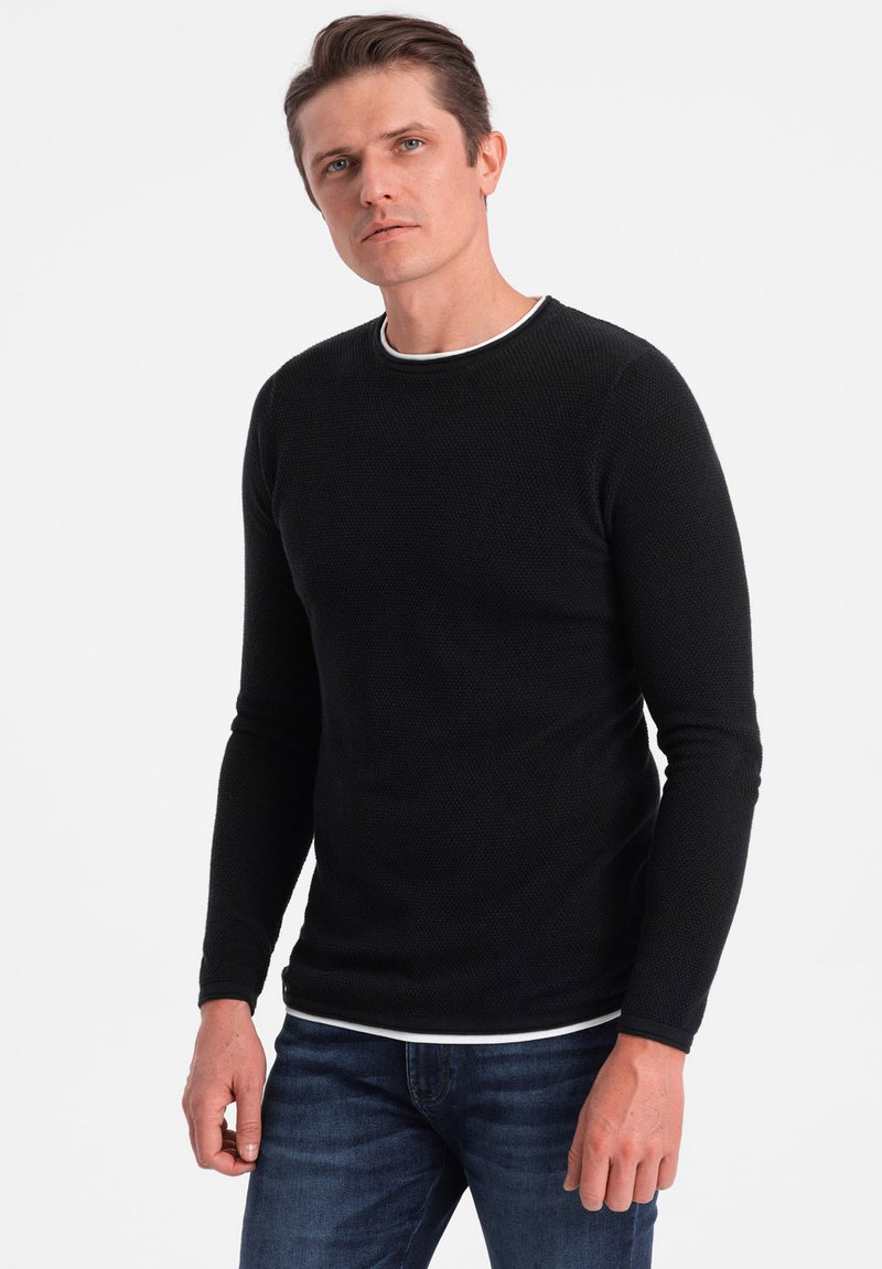 Black long-sleeve sweater with a textured fabric, round neckline edged in white, paired with blue denim jeans. No additional details.