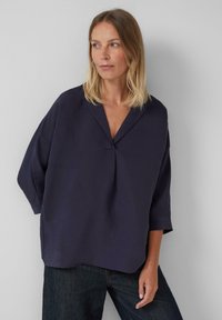 Blouse ample bleu marine avec un col en V et un détail plissé à l'avant. Manches longues avec une silhouette décontractée, fabriquée en tissu doux.