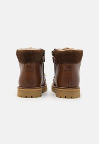Botas de cuero marrón hasta el tobillo con un cuello de gamuza marrón texturizada, forro de piel de borrego y suela de goma con un dibujo de tacos para tracción.