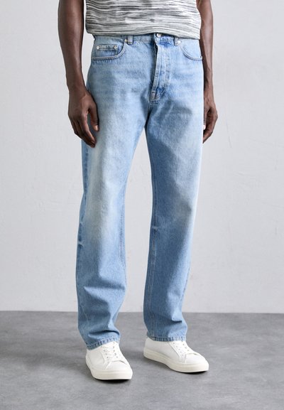 Vaqueros de mezclilla azul claro con un corte recto, que cuentan con bolsillos frontales, un acabado desgastado y detalles de costura a lo largo de las piernas. Zapatillas blancas puestas.