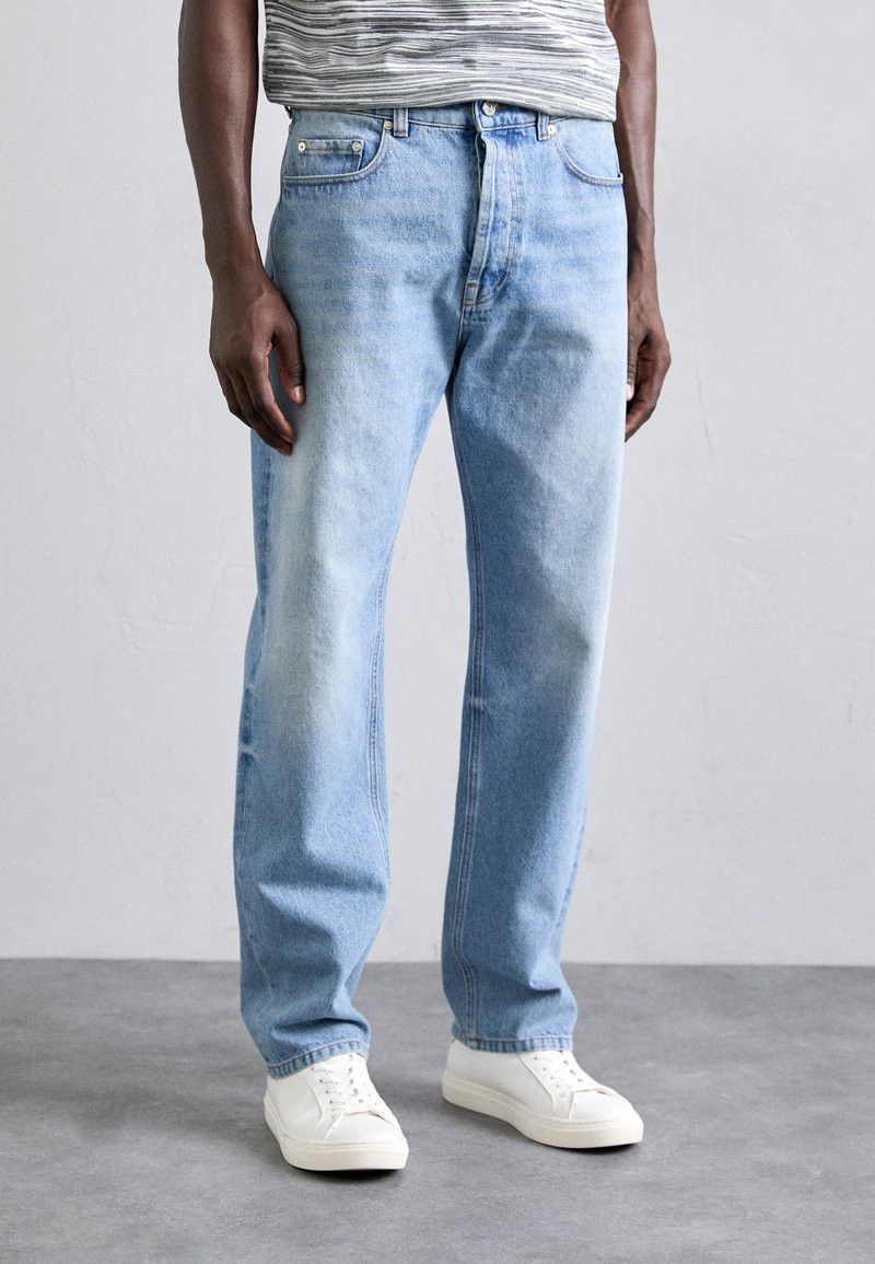 Light blue denim jeans with a straight fit, featuring front pockets, a faded finish, and stitched detailing along the legs. White sneakers worn.