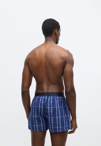 Moške kopalne hlače temno modre barve s karo vzorcem, z elastičnim črnim pasom. Lahka tkanina z gladko teksturo.