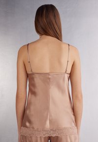 Satin camisole i mjuk tan med justerbara band, prydd med delikat spetsdetalj vid nederkanten. Slät textur med rak ryggdesign.