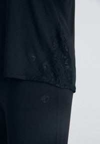 Svart topp med spetsdetaljer på fållen, tillsammans med matchande svarta leggings, båda tillverkade av ett slätt tyg med en lätt lyster.