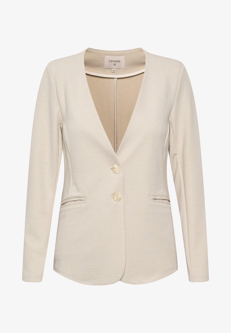 Blazer beige clair avec un profond décolleté en V, manches longues, deux poches avant et petits boutons crème. Texture de tissu lisse, coupe ajustée.