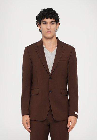 Sacou maro cu un design elegant, închidere cu un singur nasture, două buzunare frontale și țesătură texturată; purtat peste un tricou gri deschis cu decolteu în V.