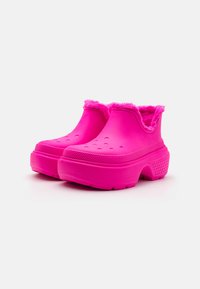 Zoccoli in gomma rosa con una soffice fodera in pelliccia sulla parte superiore, dotati di fori di ventilazione e suola con grip testurizzato per una migliore aderenza.