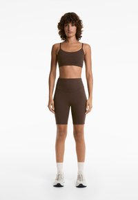 Brown sleeveless crop top and high-waisted bike shorts. Soft, stretchy fabric with no visible patterns. Accompanied by light athletic shoes.