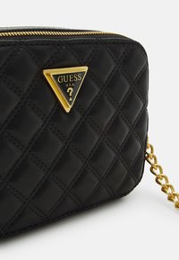 Schwarze, gesteppten Kunstledertasche mit goldfarbenem dreieckigem Logo und Kettenriemen. Reißverschluss oben.
