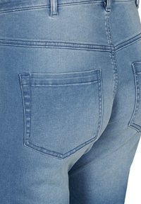 Jeans de denim azul con un diseño de cintura alta, dos bolsillos traseros y costuras cosidas, con una textura suave y ligeramente descolorida.