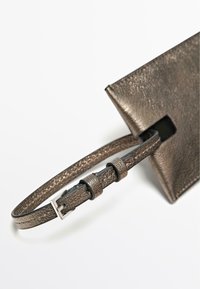 Metalická bronzová kabelka s texturovaným povrchem, která má tenký řemínek, stříbrné kování a výrazný úhlový výřez na otevření.