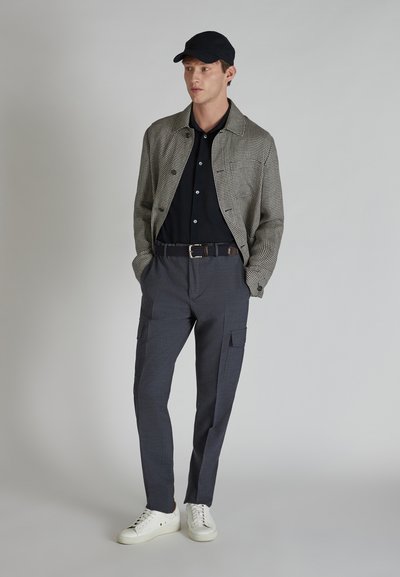 Szara, w kratkę kurtka na czarnym polo, połączona z ciemnymi spodniami cargo i białymi trampkami. Klapka dopełnia strój. Czyste linie i tekstury.