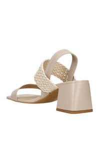 Sandalo con tacco beige caratterizzato da cinturini intrecciati, un tacco quadrato e dettagli in pelle liscia sulla soletta e sui cinturini.