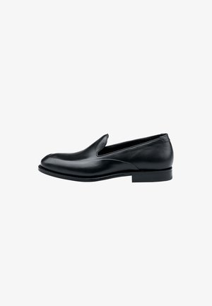 Zwarte leren instapper met lage hak, gladde afwerking en slip-on ontwerp, van opzij gezien tegen een witte achtergrond.