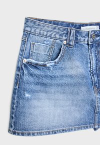 Jupe en jean bleu clair, avec des détails déchirés, une poche avant et des accents en métal sur la taille et le bouton.