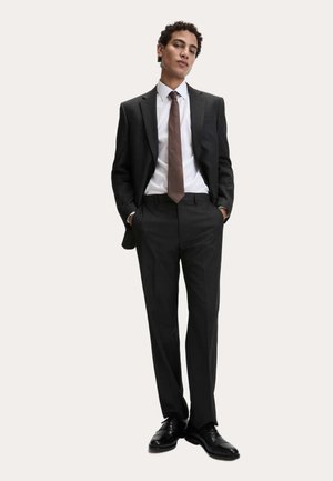 Mørkegråt skræddersyet jakkesæt med en hvid skjorte med knapper og et tekstureret brunt slips. Sorte lædersko fuldender det formelle outfit.