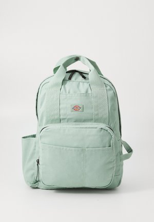 Hellgrüner Canvas-Rucksack mit vorderer Reißverschlusstasche, Seitentasche, doppelten Griffen mit Druckknopf und kleinem Logo-Patch vorne in der Mitte.