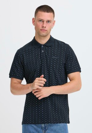 Sort polo-shirt med et tekstureret mønster, der indeholder små blå geometriske figurer, to-knaps stolpelukning og kontrasterende krave.