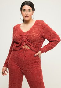 Rustfarbenes Strickoberteil und passende Hose mit einer offenen Strickmuster, V-Ausschnitt und verstellbarem Kordelzug in der Taille.