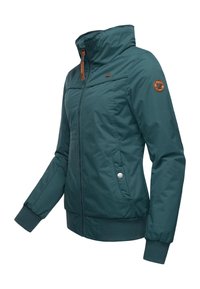 Blågrøn lynlåsjakke med høj krave, ribstrikkede manchetter og kant. Har sidelommer og en brun logopatch på venstre ærme. Glat tekstur.