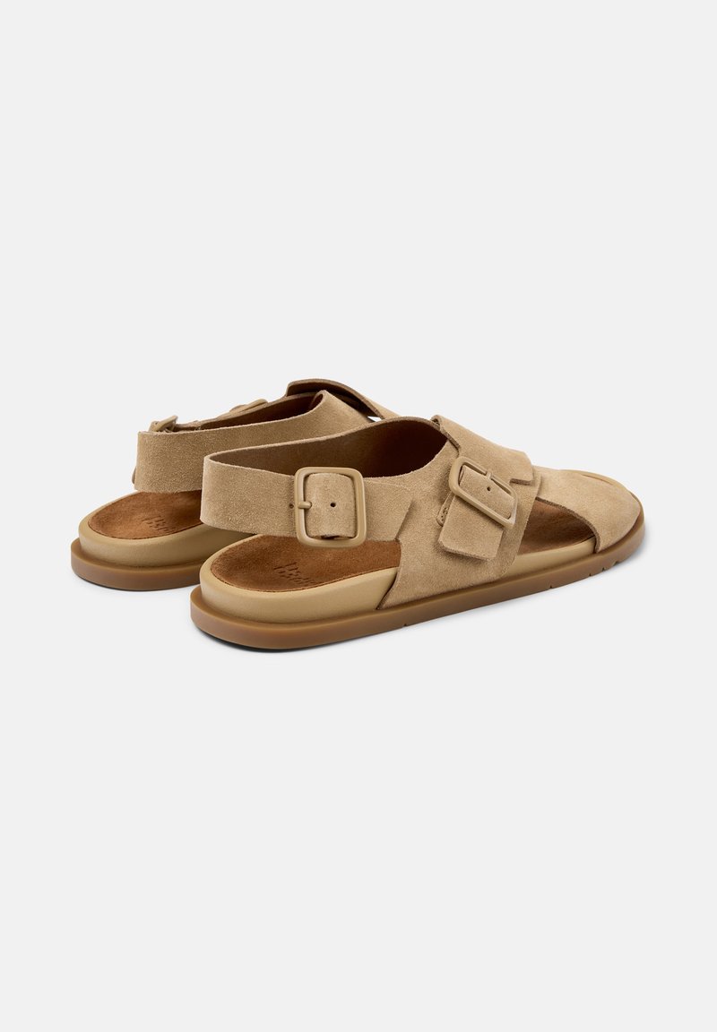 Par de sandalias de ante color marrón claro con correas ajustables con hebilla y suelas acolchadas sobre un fondo liso gris claro.