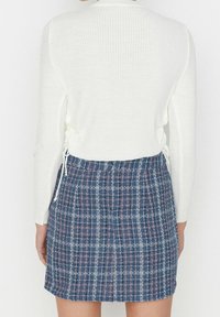 Haut blanc à manches longues côtelé avec côtés à cordon, associé à une mini-jupe à carreaux bleus avec des accents roses et blancs, tissu texturé.