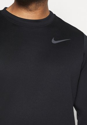 Gros plan d'une personne portant un t-shirt Nike noir avec un logo Nike swoosh gris sur la partie supérieure de la poitrine.