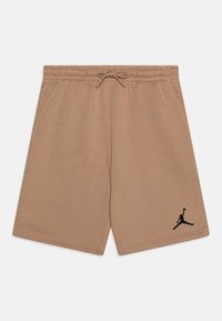 Béžové šortky z měkké látky; mají elastický pas se šňůrkou a černé logo Jumpman na levé noze.