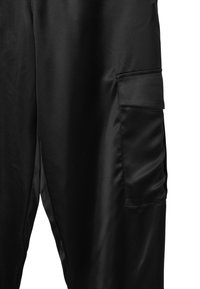 Pantaloni neri in satin con una tasca a pattina sulla coscia, mostrando una texture di tessuto liscia e dettagli di cucitura raffinati.