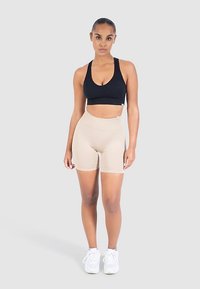 Mustat urheiluliivit ja ihonväriset, korkeavyötäröiset shortsit henkilöllä. Shortsit ovat joustavat ja istuvat, kun taas liivien muotoilu on yksinkertainen ja molemmat ovat yksivärisiä.