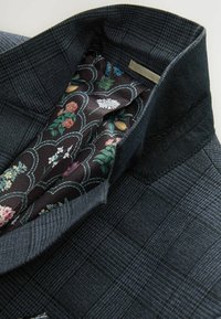 Sacou cu carouri închise, realizat dintr-un material exterior texturat. Interiorul prezintă o căptușeală cu un model floral pe un fundal închis.