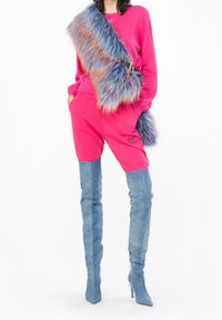 En ljusrosa sweatshirt och shorts med broderad logotyp, tillsammans med höga blå denimstövlar som går upp till låren och en flerfärgad fuskpälsväska.