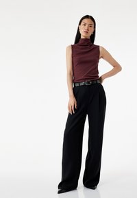 Bordeaux mouwloze top met een hoge nek, gecombineerd met zwarte op maat gemaakte wijde broek. Glanzende zwarte riem met een rechthoekige gesp.