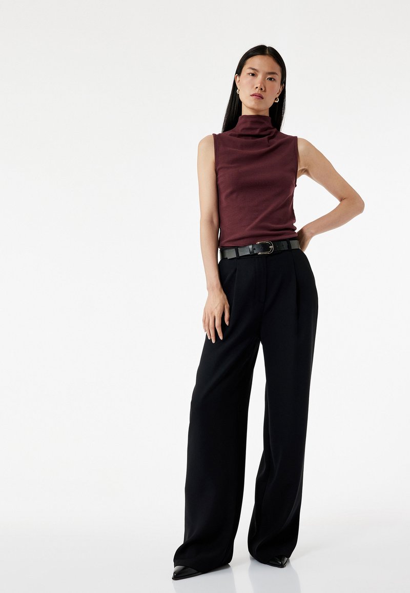 Bordeaux mouwloze top met een hoge nek, gecombineerd met zwarte op maat gemaakte wijde broek. Glanzende zwarte riem met een rechthoekige gesp.