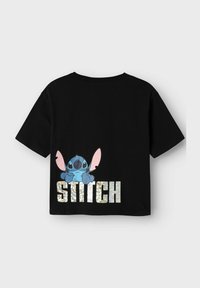 T-shirt en coton noir avec un personnage de cartoon coloré aux grandes oreilles et le mot "STITCH" en lettres brillantes au dos.