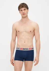 Tumši zili bokserbikses ar baltas un sarkanas Diesel logo gumiju. Audums izskatās gluds un elastīgs, cieši pieguļ ķermenim.