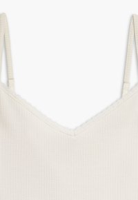 Camisole côtelée couleur crème avec fines bretelles réglables et bordure en dentelle festonnée le long du décolleté.