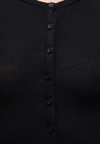 Gros plan d'un vêtement en tissu côtelé noir avec une rangée verticale de sept boutons noirs fermés au centre.