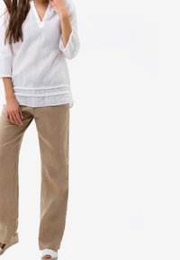 Vit linneöverkappa med trekvartsärmar, med V-ringning och lager av fåll, i kombination med beige vida linnebyxor.