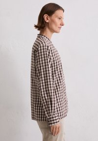 Brown and cream checked button-up shirt with long sleeves and a collar, crafted from a textured fabric. Side profile view.